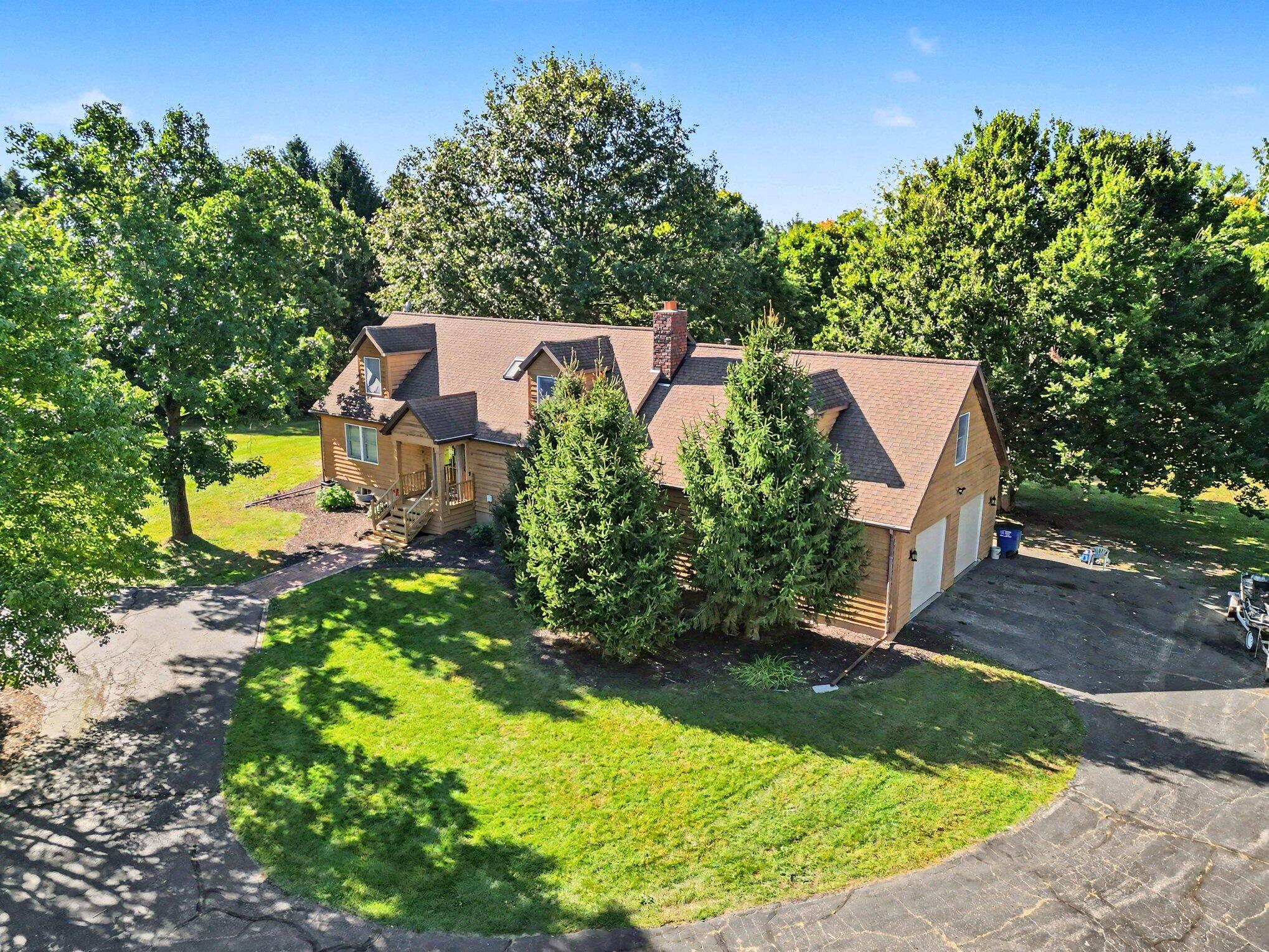 Aerial view of a wood-sided house with an attached garage, mature trees, and a broad lawn.