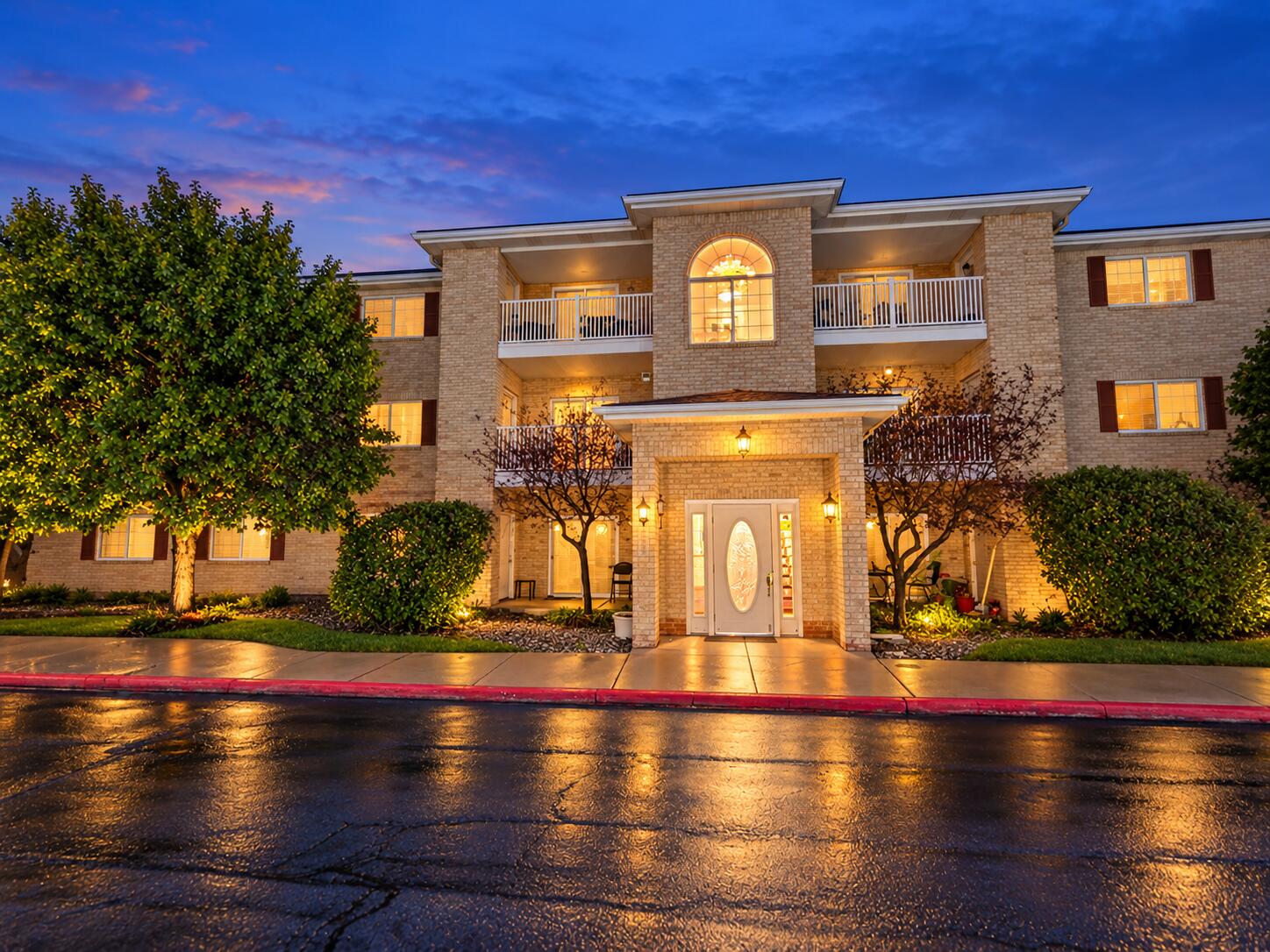 Two-story brick building with balconies and a warmly lit entrance at dusk.