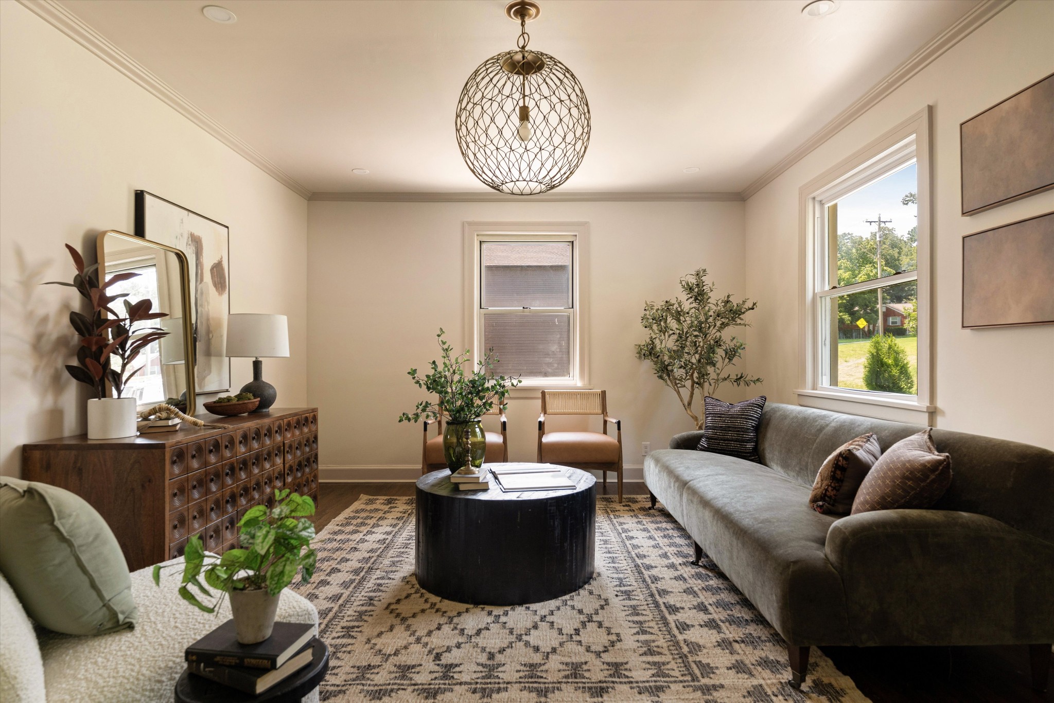 Staged living room with a gray sofa, round black coffee table, patterned rug, and large windows.