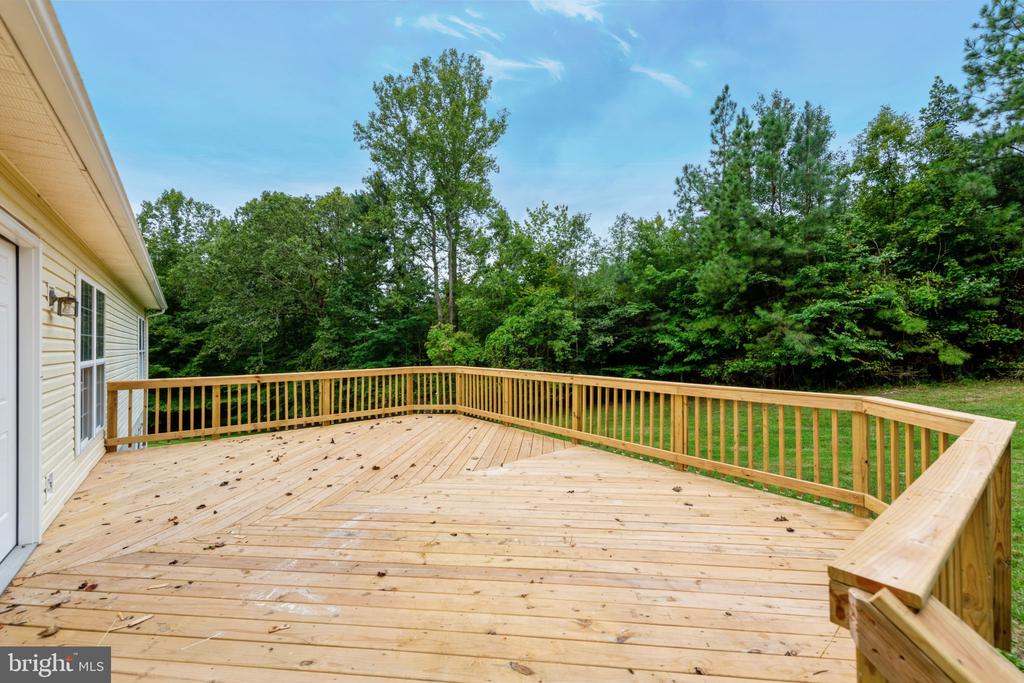 Large wooden deck with railings overlooking a lawn and dense trees.