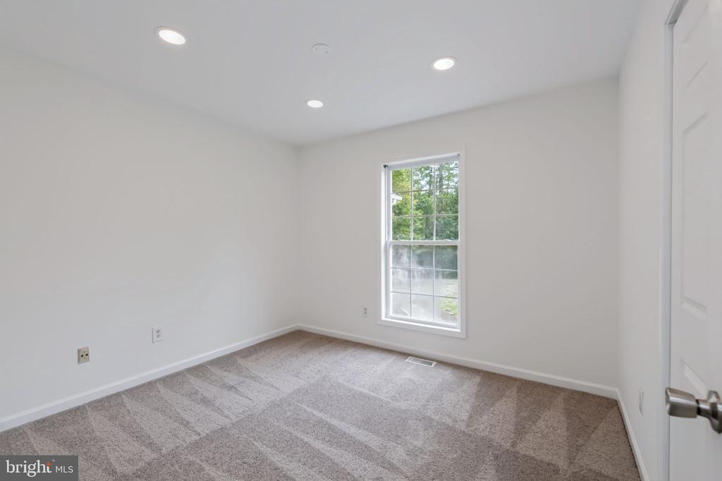 Empty carpeted room with recessed lights and a window overlooking greenery.