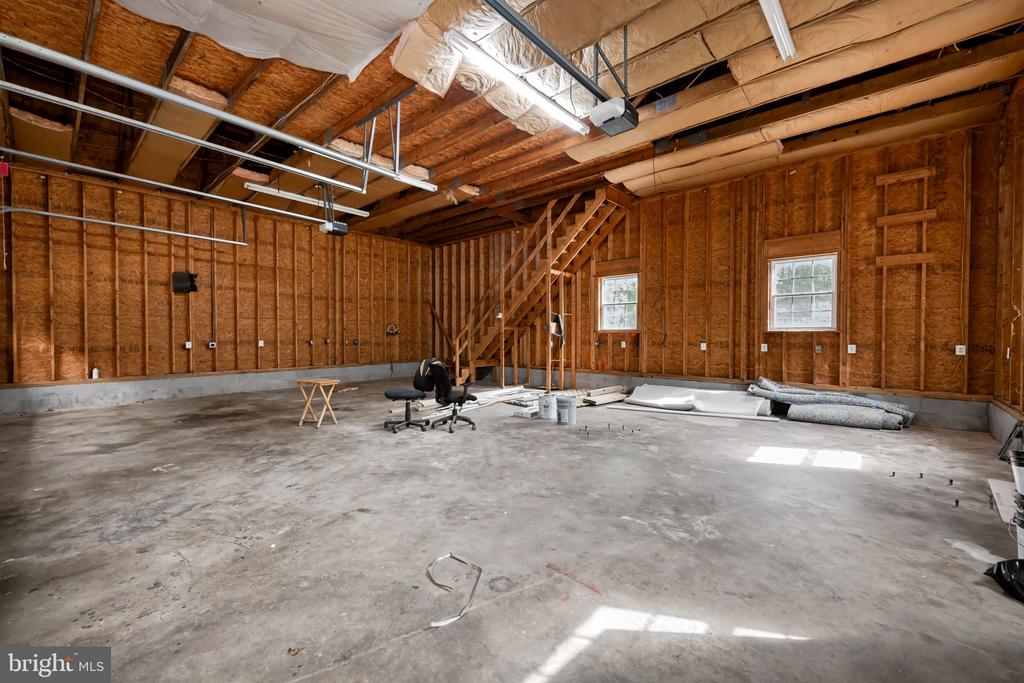 Unfinished garage with exposed framing, concrete floor, and staircase to an upper level.