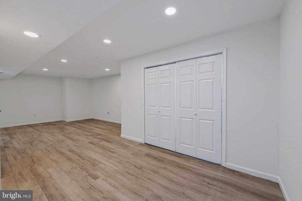 Empty finished room with wood-look flooring, recessed lights, and white folding closet doors.