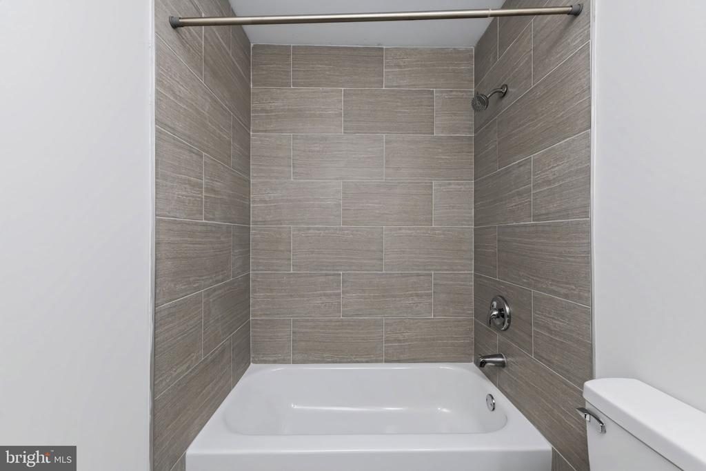 Bathroom with a white bathtub, gray tiled shower surround, and chrome fixtures.