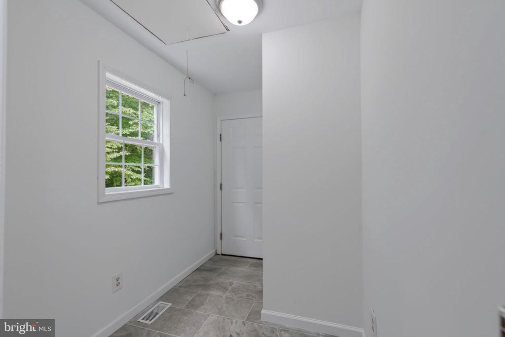 Empty utility room with gray tile flooring, a multi-pane window, and a closed white door.