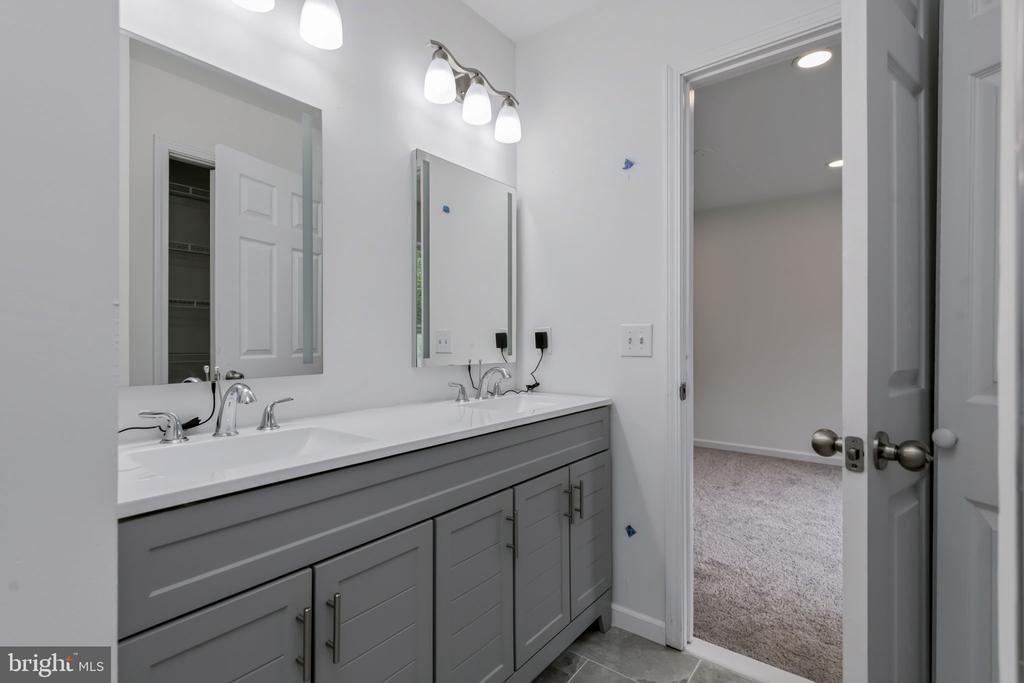 Bathroom with a double-sink vanity, gray cabinetry, and two mirrors beside an open doorway.