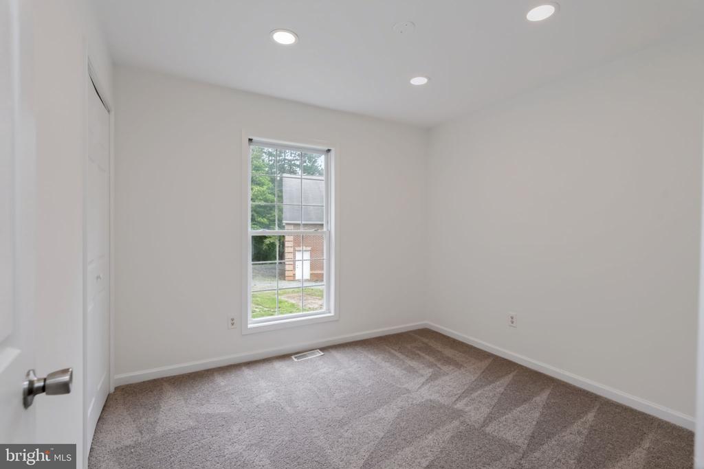 Empty bedroom with neutral walls, patterned carpet, recessed lights, and a window overlooking greenery.