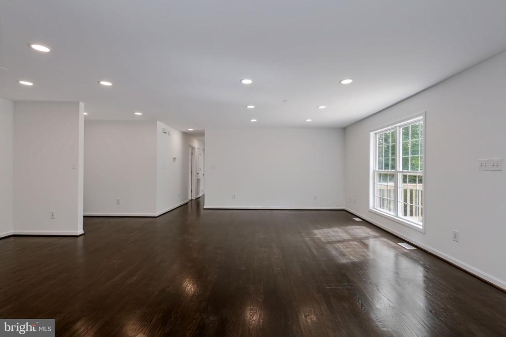 Empty living room with dark hardwood floors, recessed lights, and a large window.