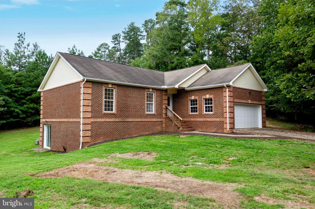 Red brick house with an attached garage, grassy lawn, and mature trees.