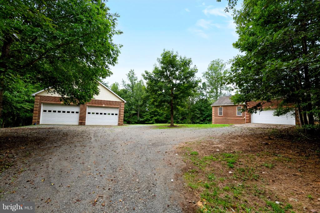 Two brick garage buildings flank a broad gravel driveway beneath mature trees.