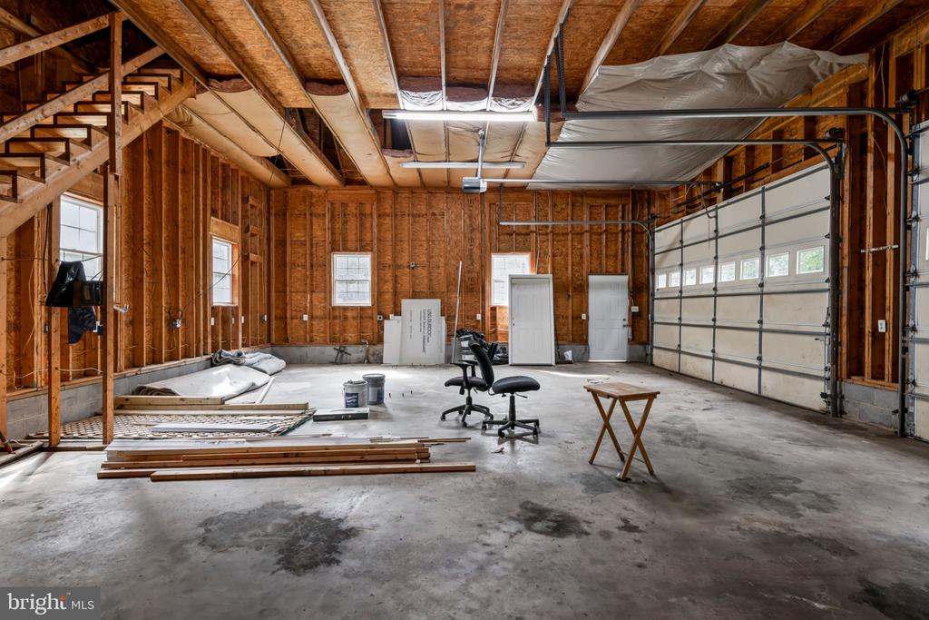 Unfinished garage with exposed wood framing, a concrete floor, and an overhead garage door.