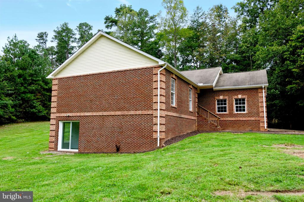Two-story brick house with a white-sided gable, sloping lawn, and mature trees.