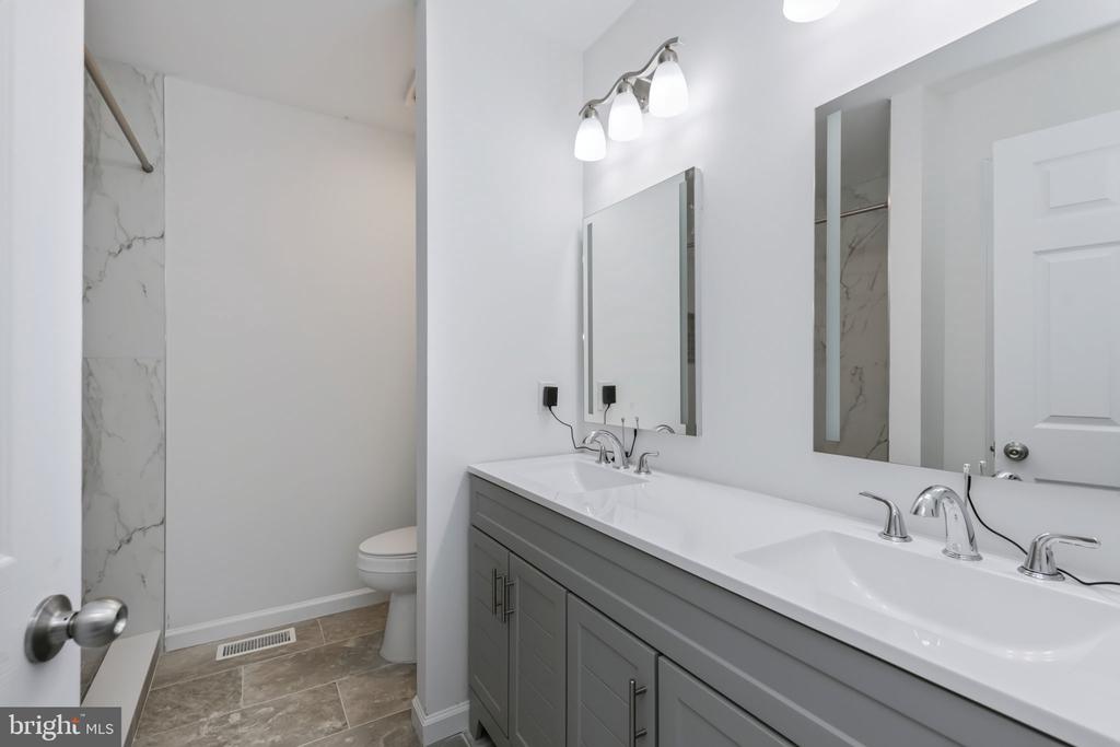 Bathroom with a long gray double-sink vanity, two mirrors, and marble-look tile.