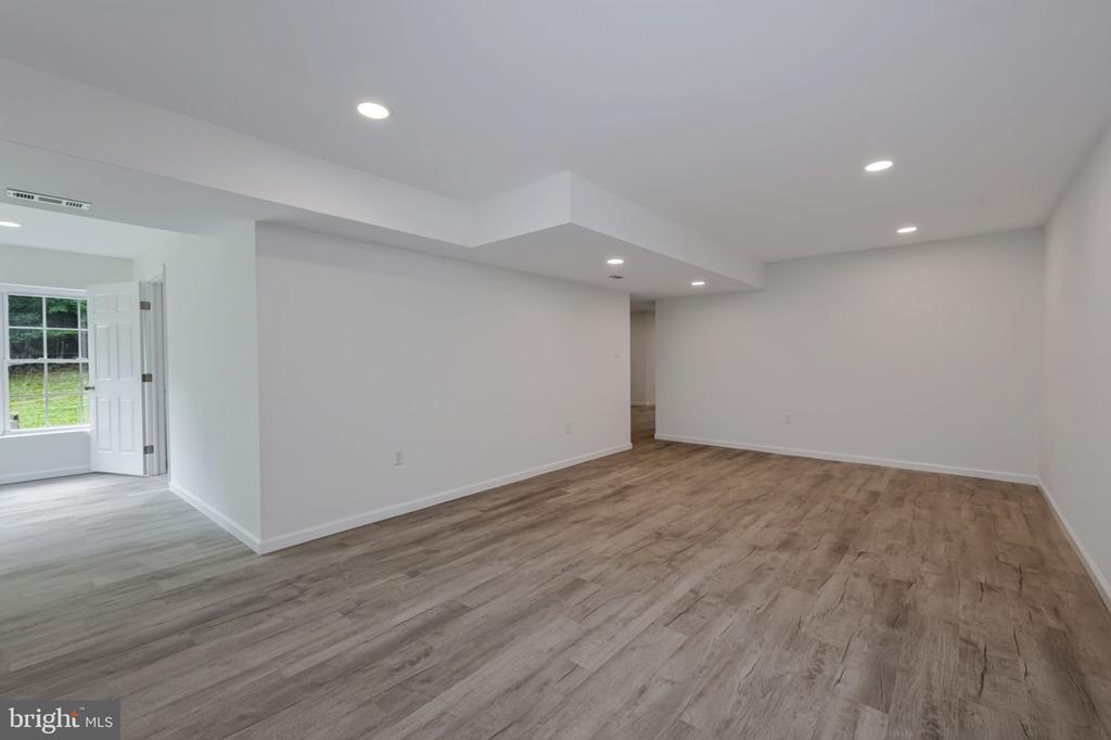 Empty finished room with wood-look flooring, recessed lights, and a windowed area through the doorway.