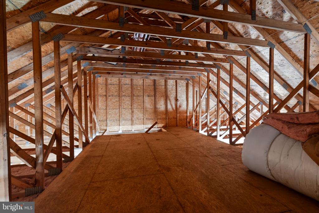 Unfinished attic with exposed roof trusses, plywood flooring, and a roll of insulation.