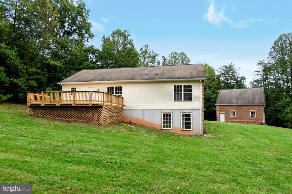 Rear of a light-sided house with a raised wooden deck and a separate brick outbuilding.