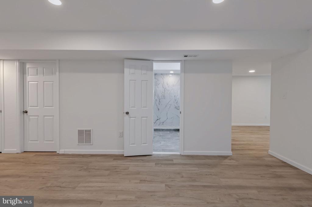 Empty room with wood-look flooring and an open doorway to a marble-look tiled room.