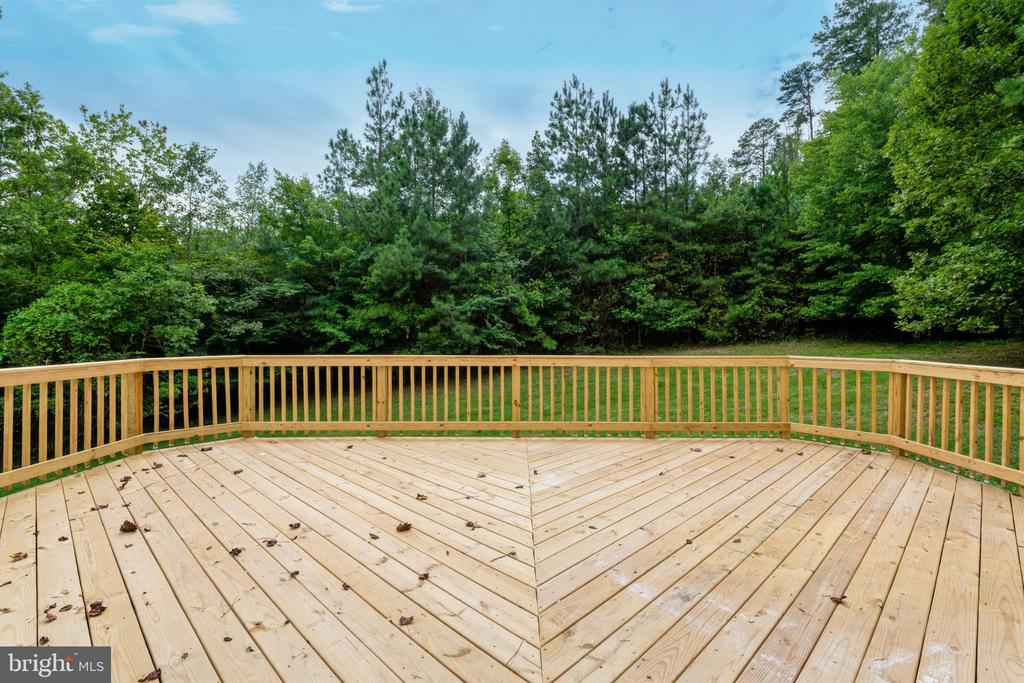 Wooden deck with a wraparound railing overlooking a dense green tree line.