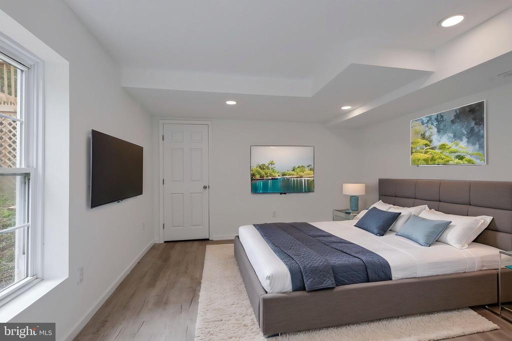 Bedroom with a gray upholstered bed, blue bedding, large window, and wall-mounted television.