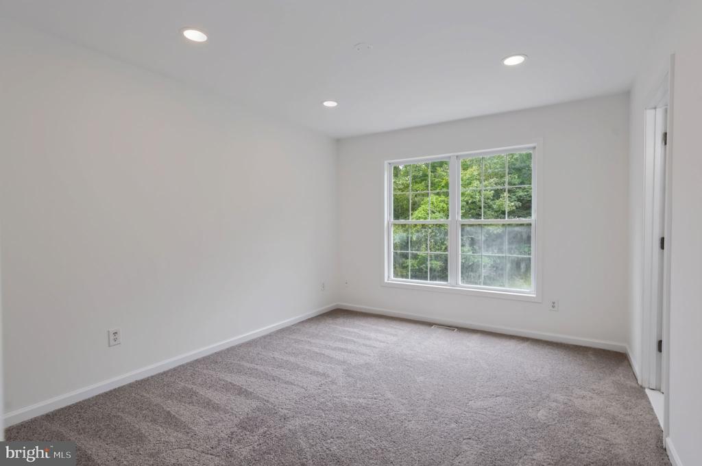 Empty carpeted bedroom with recessed lights and a wide window overlooking greenery.