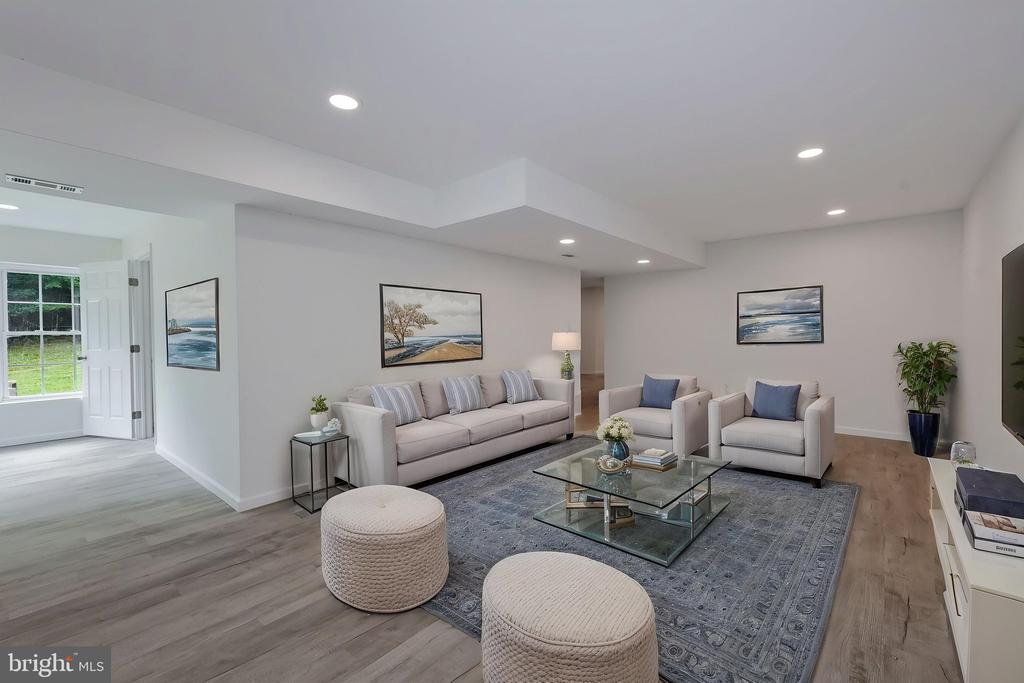 Staged living room with a gray sofa, two armchairs, glass coffee table, and coastal artwork.