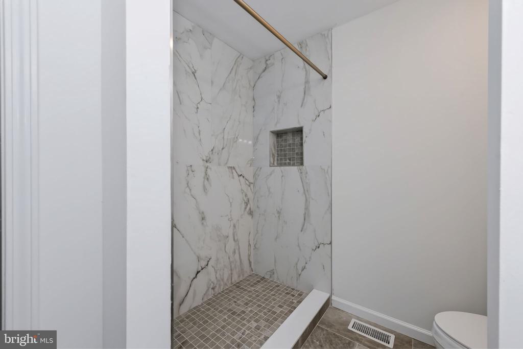 Marble-look tiled shower with a glass-tile niche and brass showerhead.