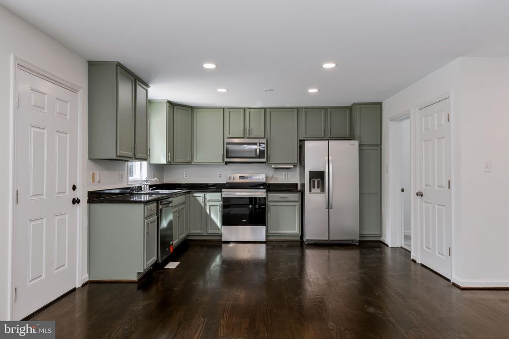 Kitchen with sage-green cabinets, stainless steel appliances, and dark wood flooring.
