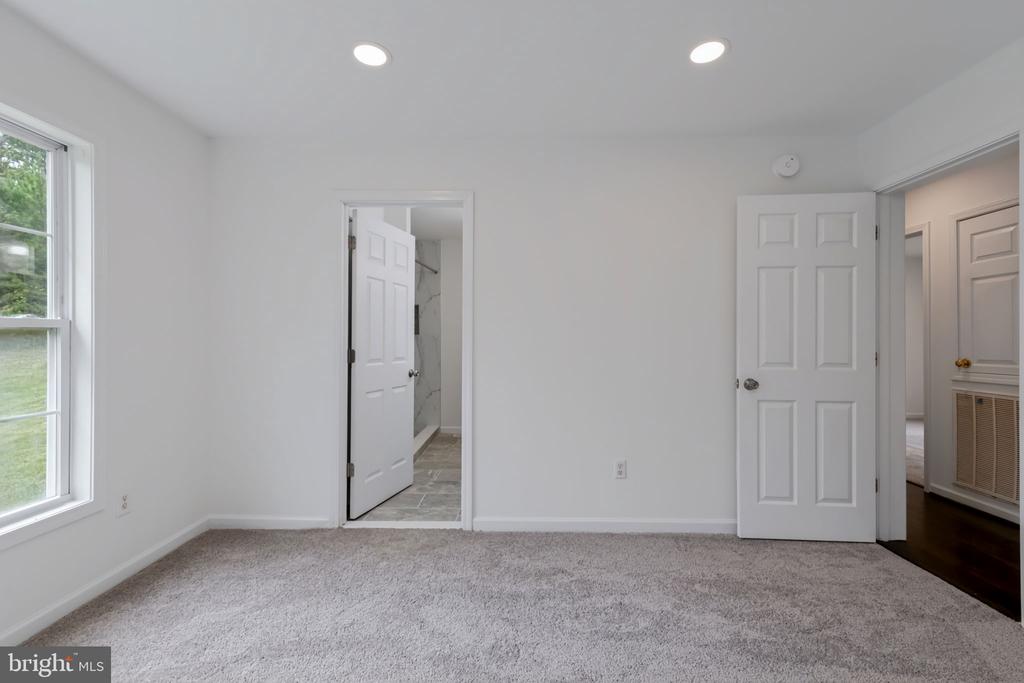 Empty carpeted bedroom with a window and open doorways to a tiled bathroom and hall.
