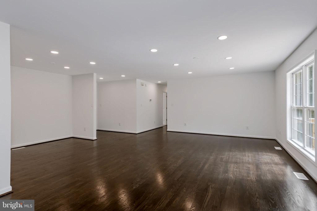 Vacant open room with dark hardwood floors, recessed lights, and tall windows.