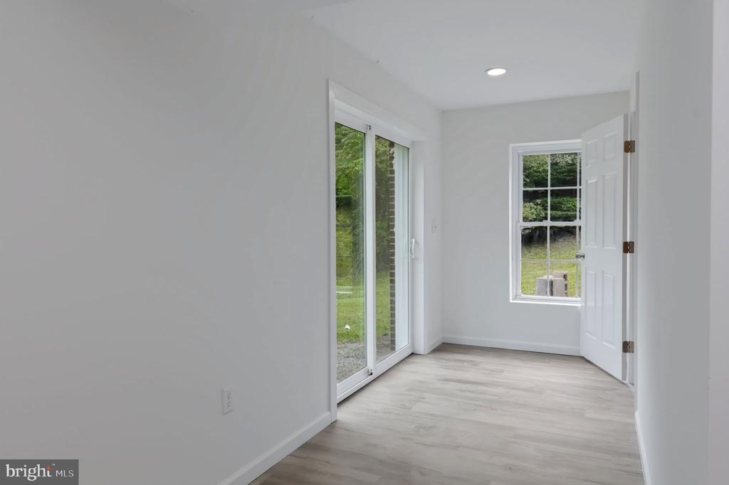 Vacant room with light wood-look floors, a sliding glass door, and a window overlooking greenery.