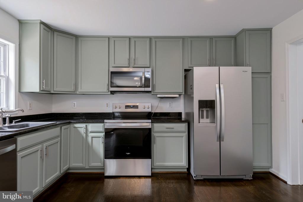 Kitchen with pale gray-green cabinets, black countertops, stainless steel appliances, and dark hardwood floors.