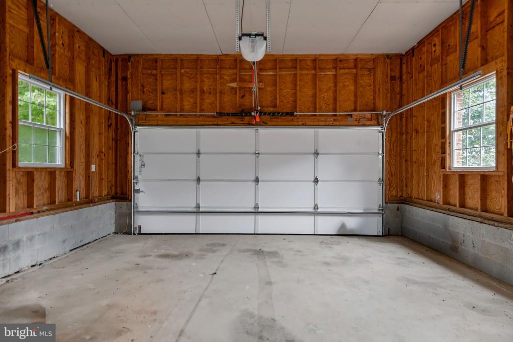 Empty garage with a wide white door, exposed wood framing, and windows on both sides.