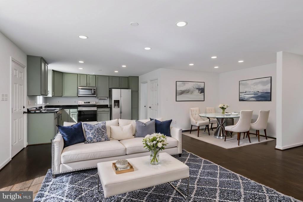 Open-plan living room with a white sofa, sage-green kitchen cabinets, and an adjoining dining area.
