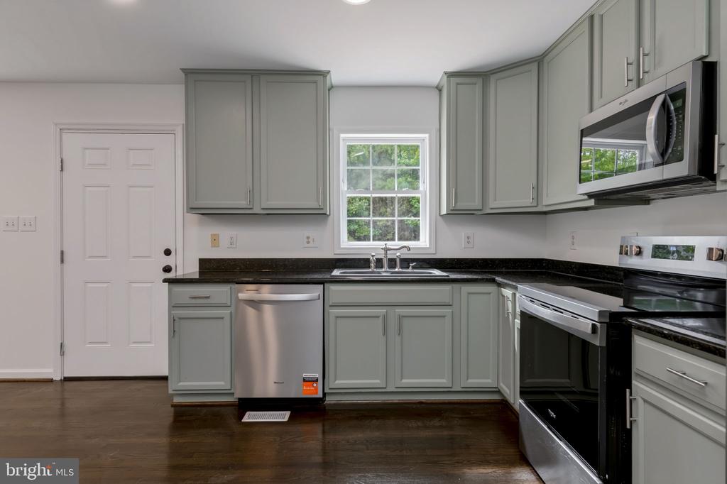 Kitchen with sage-gray cabinets, dark countertops, stainless-steel appliances, and a window above the sink.