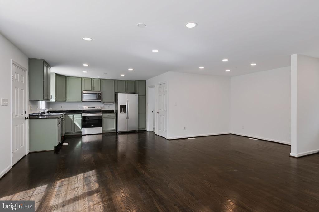 Open-plan kitchen and living area with sage-green cabinets, stainless steel appliances, and dark hardwood floors.