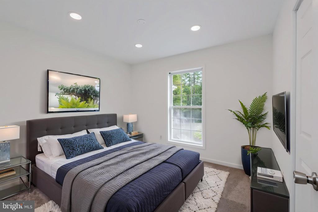 Staged bedroom with a gray upholstered bed, blue bedding, window, and wall-mounted television.