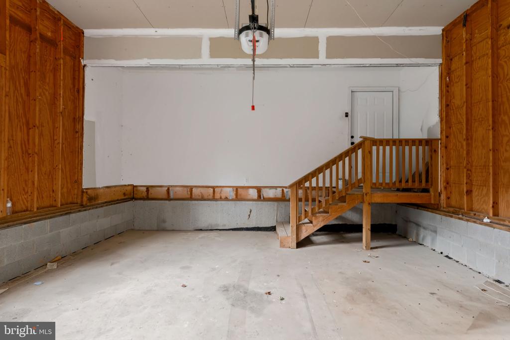 Unfinished garage with a concrete floor and wooden stairs leading to a raised platform.