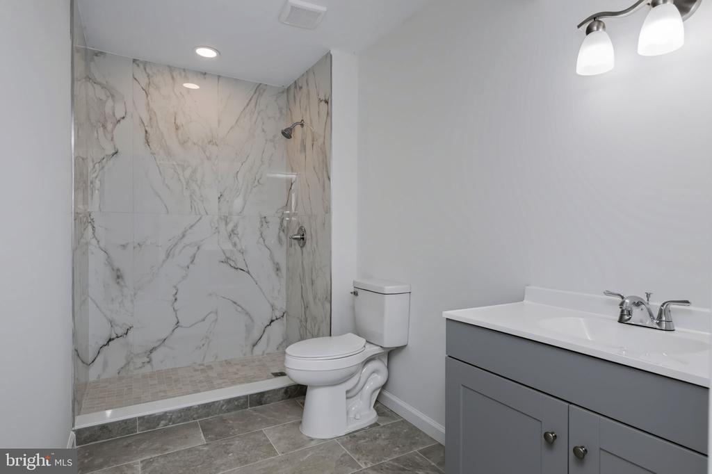 Bathroom with a marble-look walk-in shower, gray vanity, and gray tile floor.