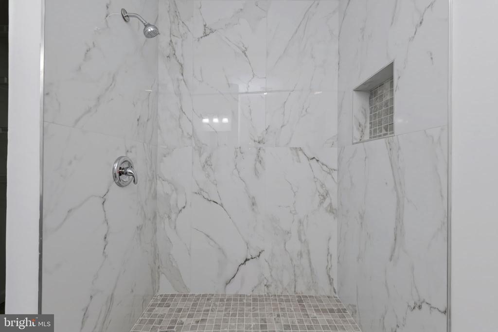 Walk-in shower with veined marble walls, mosaic floor, and recessed glass-block niche.