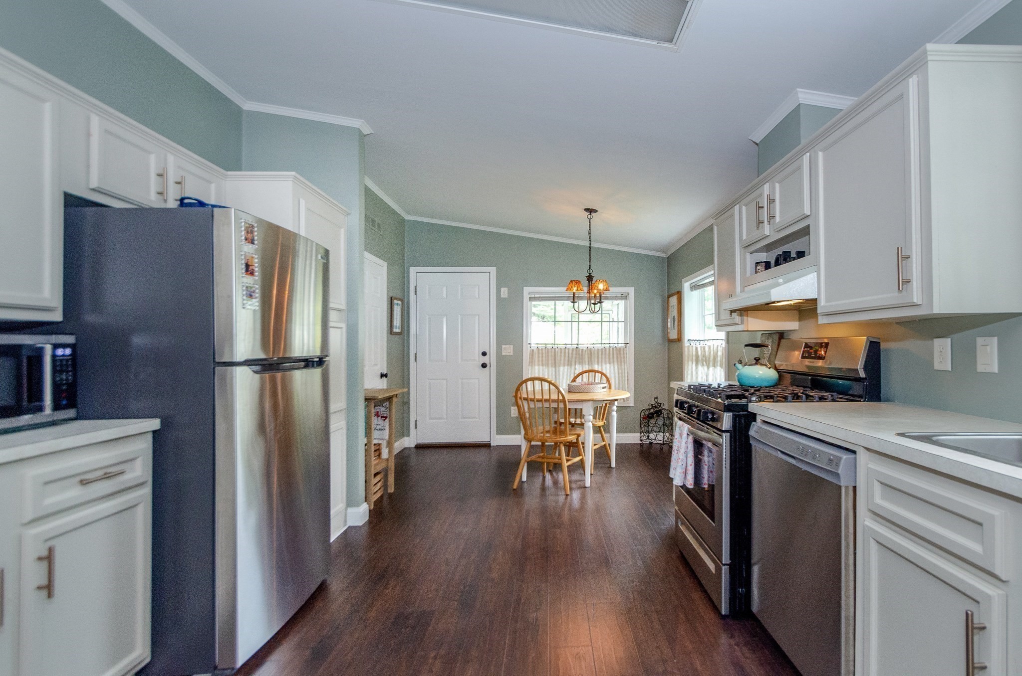 Kitchen with white cabinets, stainless steel appliances, and a small dining table by the windows.