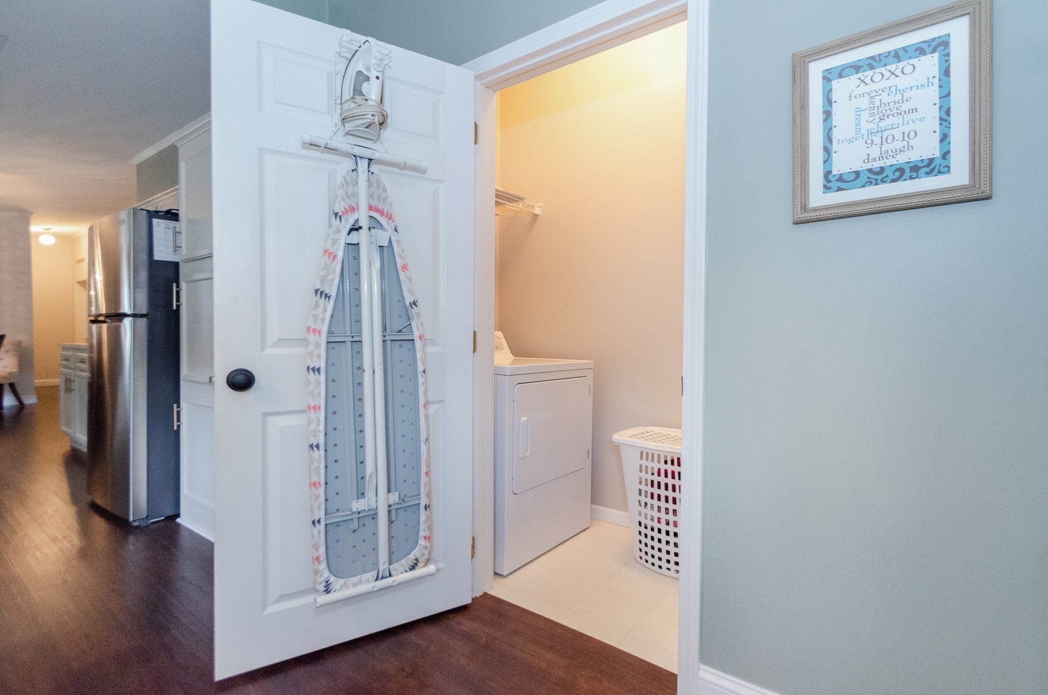 Laundry area with a dryer, laundry basket, and ironing board hanging on the open door.