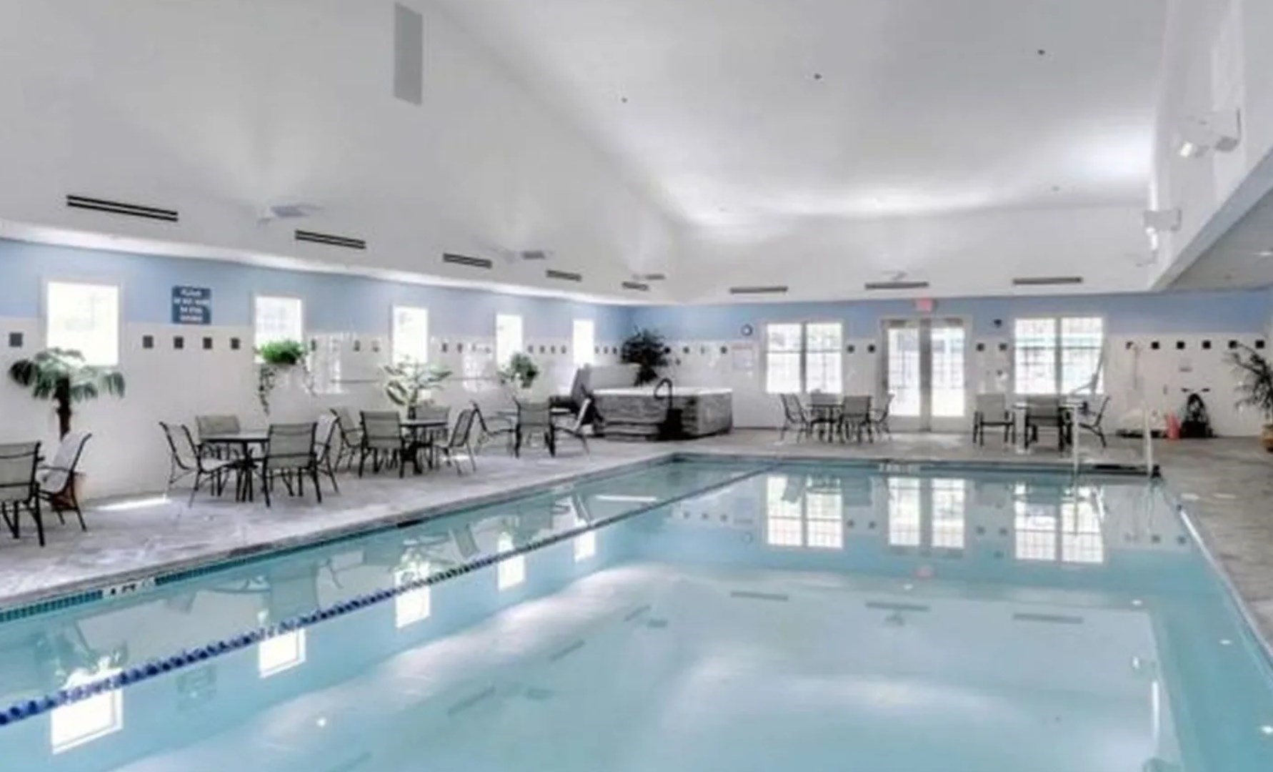 Indoor swimming pool with lane markings and a tiled deck furnished with tables and chairs.