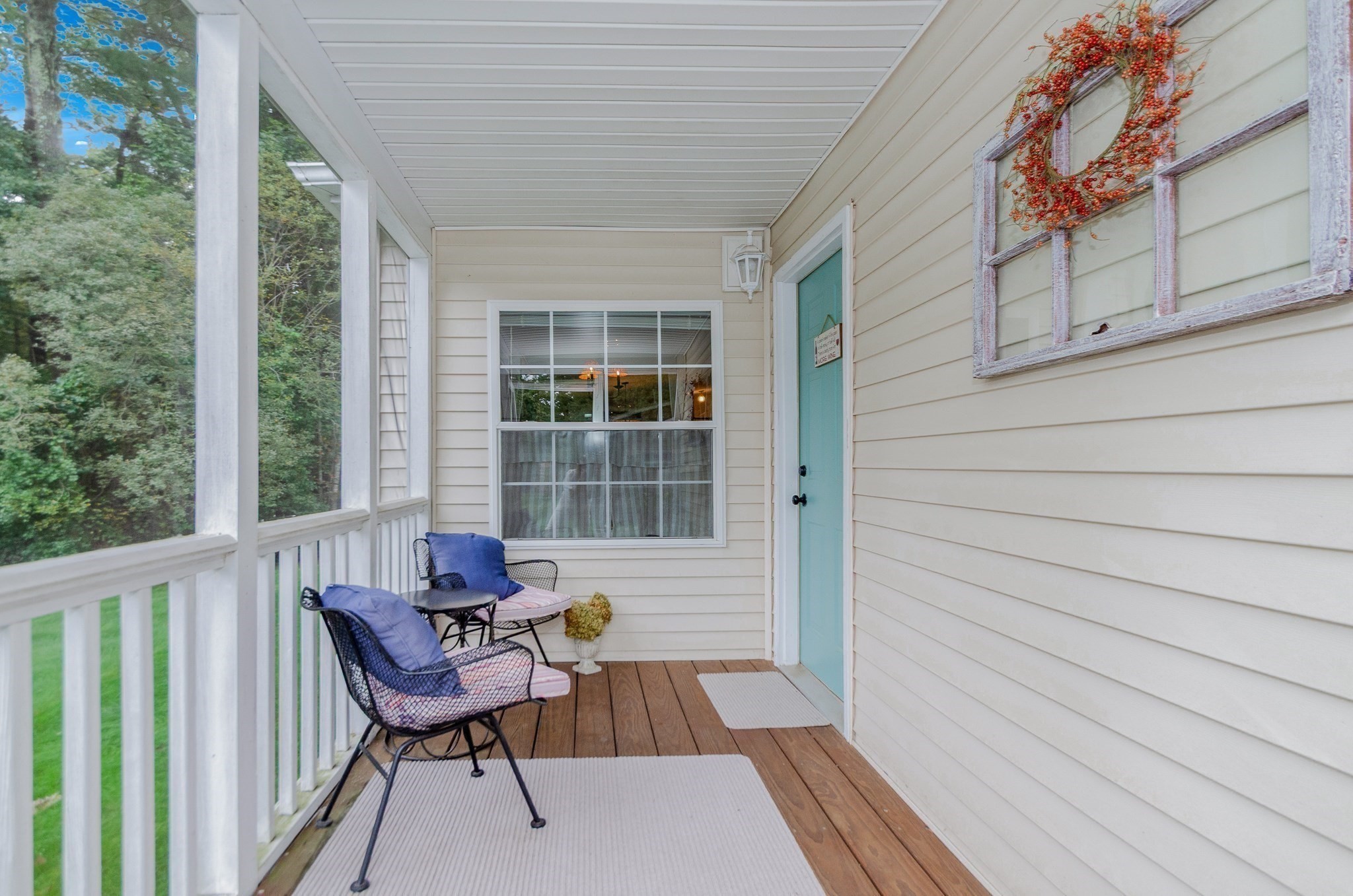 Covered porch with a turquoise door, wood flooring, and black metal chairs with blue cushions.