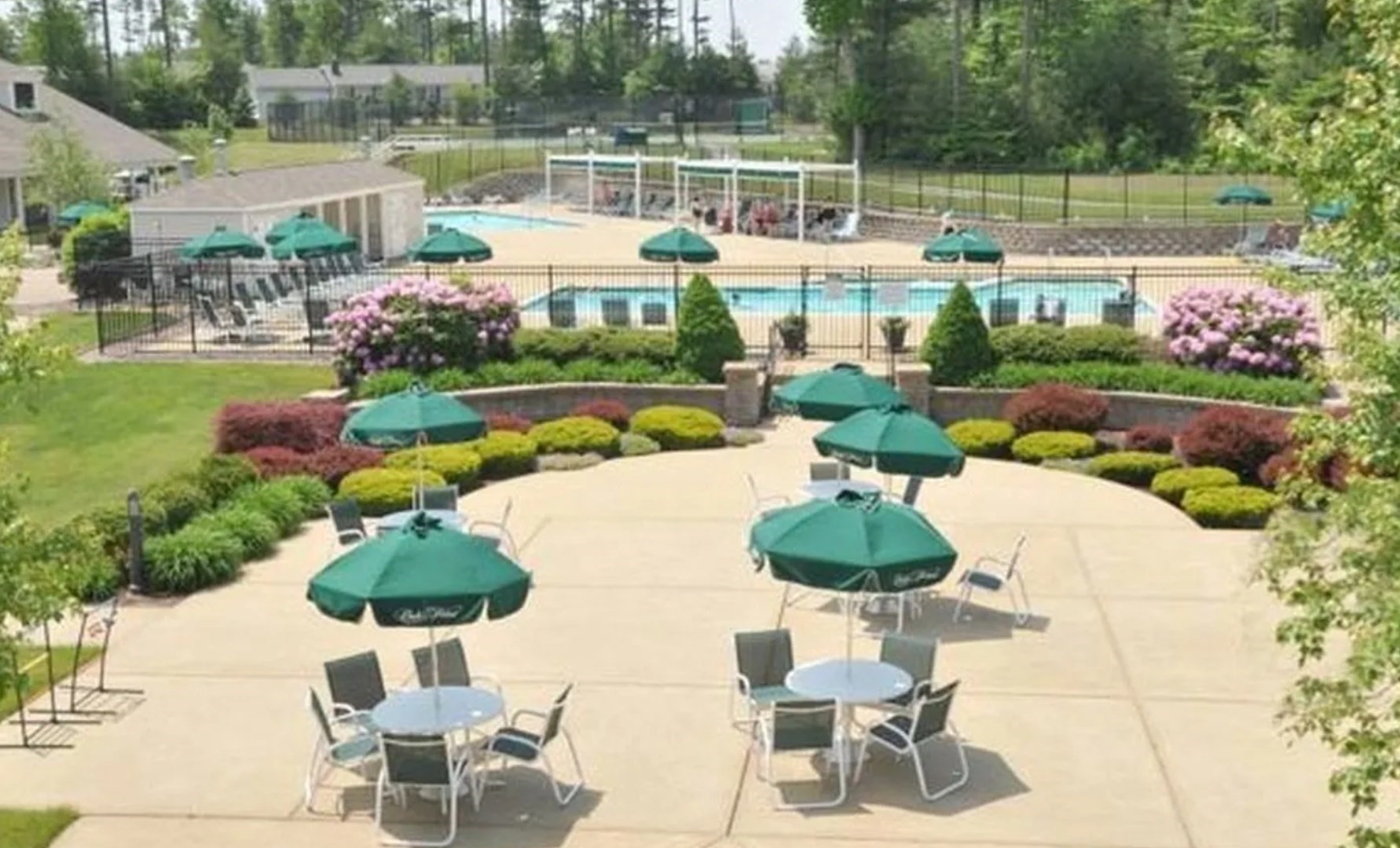 Outdoor swimming pool behind a landscaped patio with green umbrellas and seating.