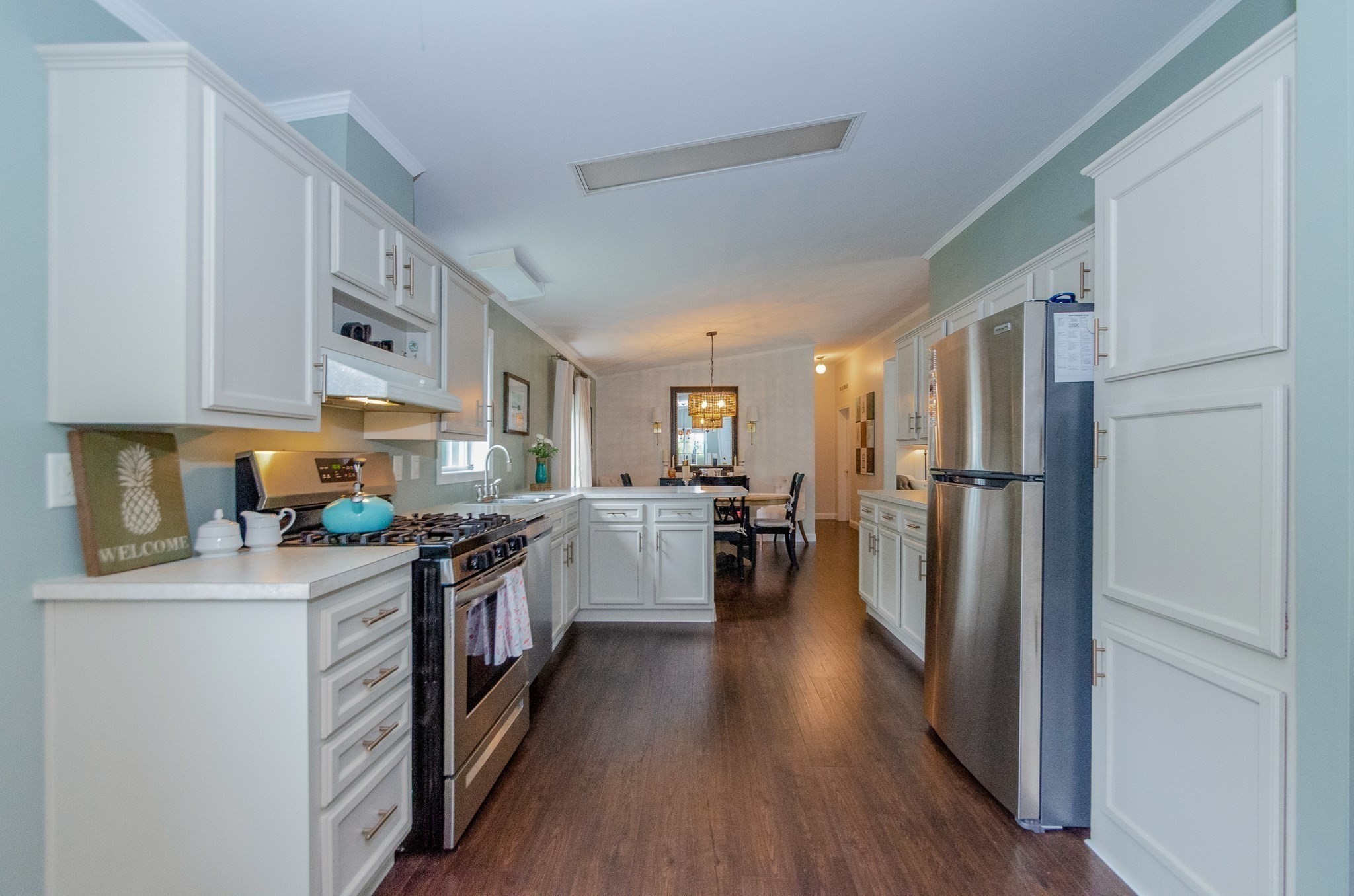 Kitchen with white cabinetry, stainless steel appliances, a gas range, and dining area beyond.