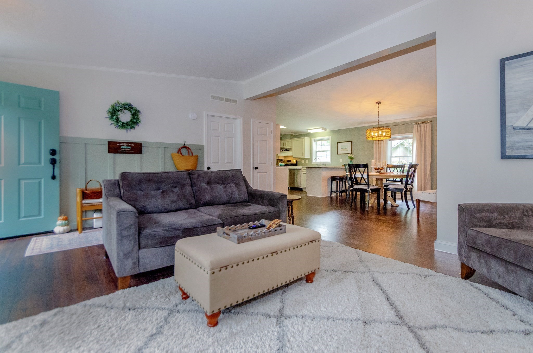 Open-plan living room with gray sofa and white rug leading to a dining area and kitchen.