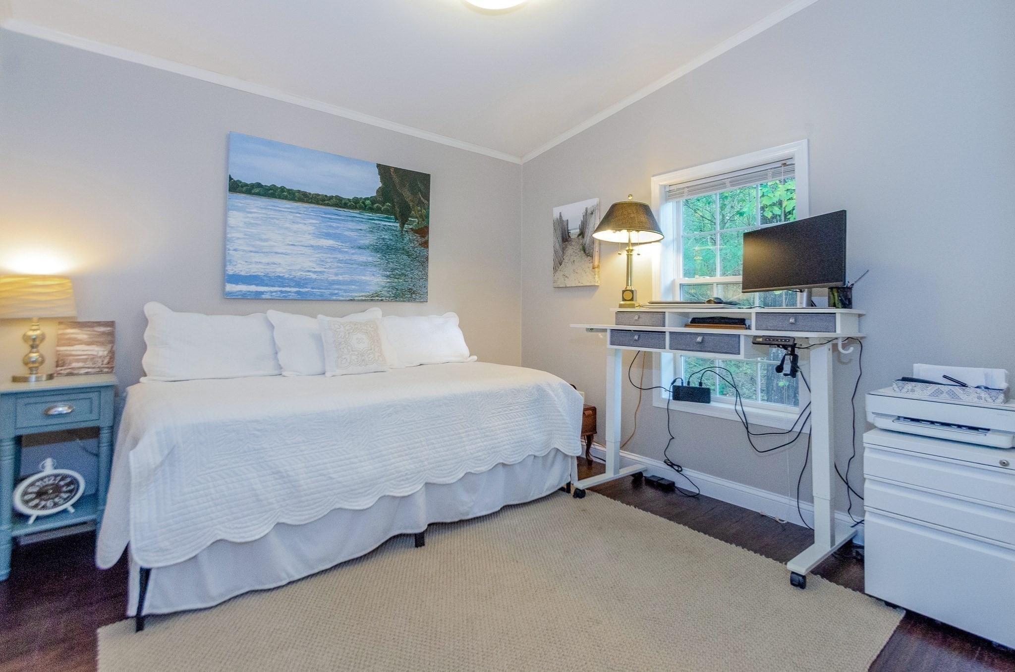 Furnished bedroom with a white bed, a desk by the window, and a beige rug.