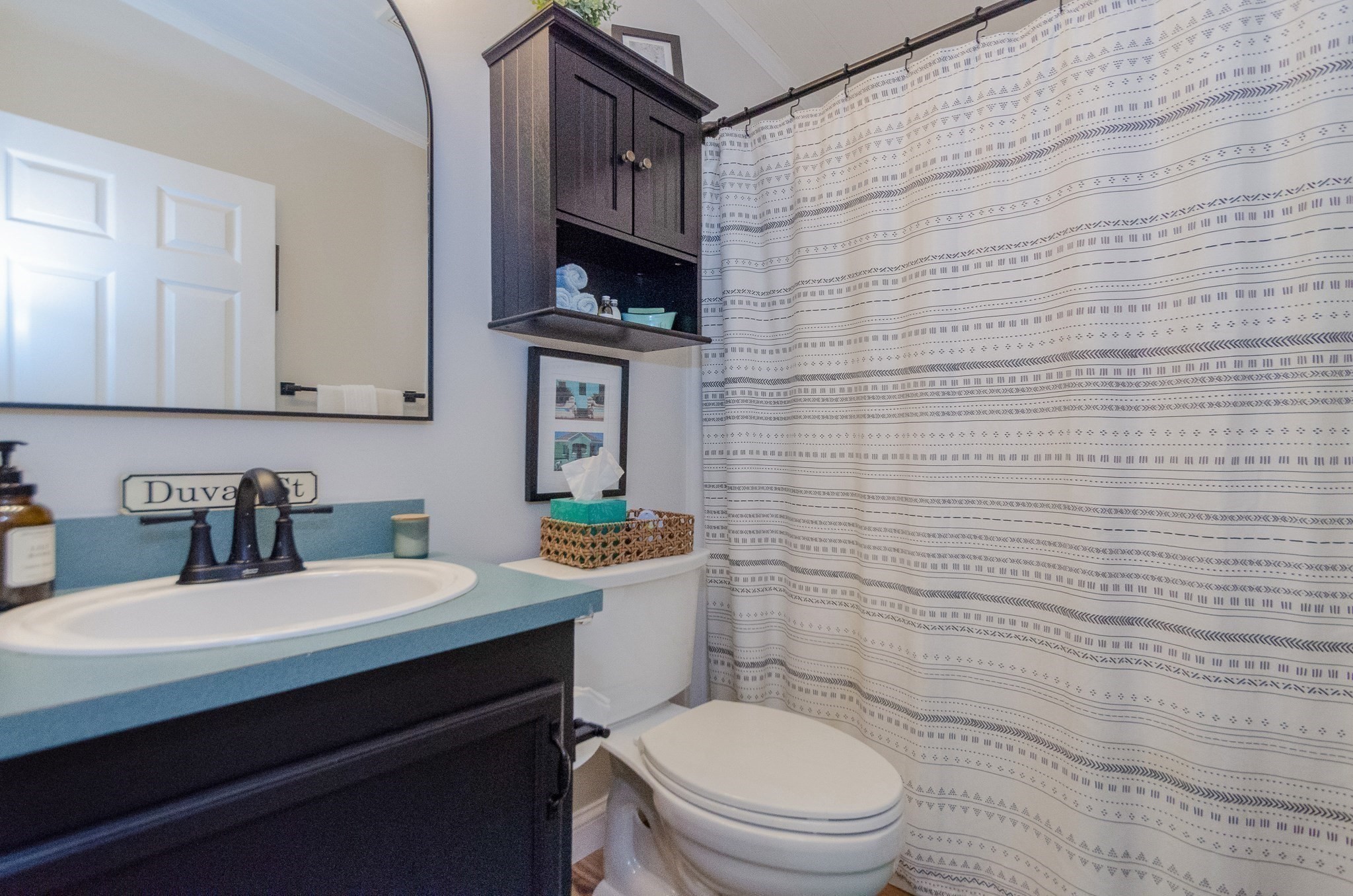 Bathroom with a blue countertop, dark vanity, wall cabinet, and patterned shower curtain.