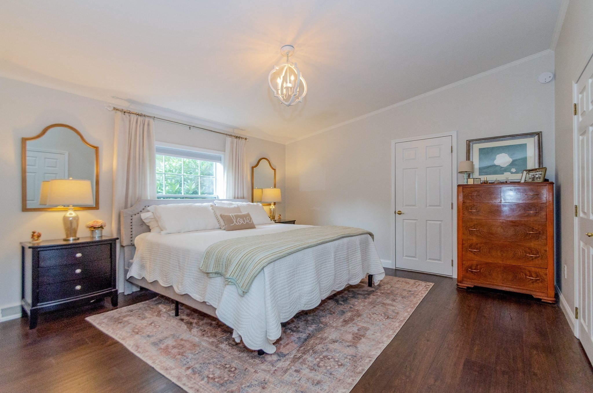 Bedroom with a white bed, patterned rug, curtained window, and wooden dresser.