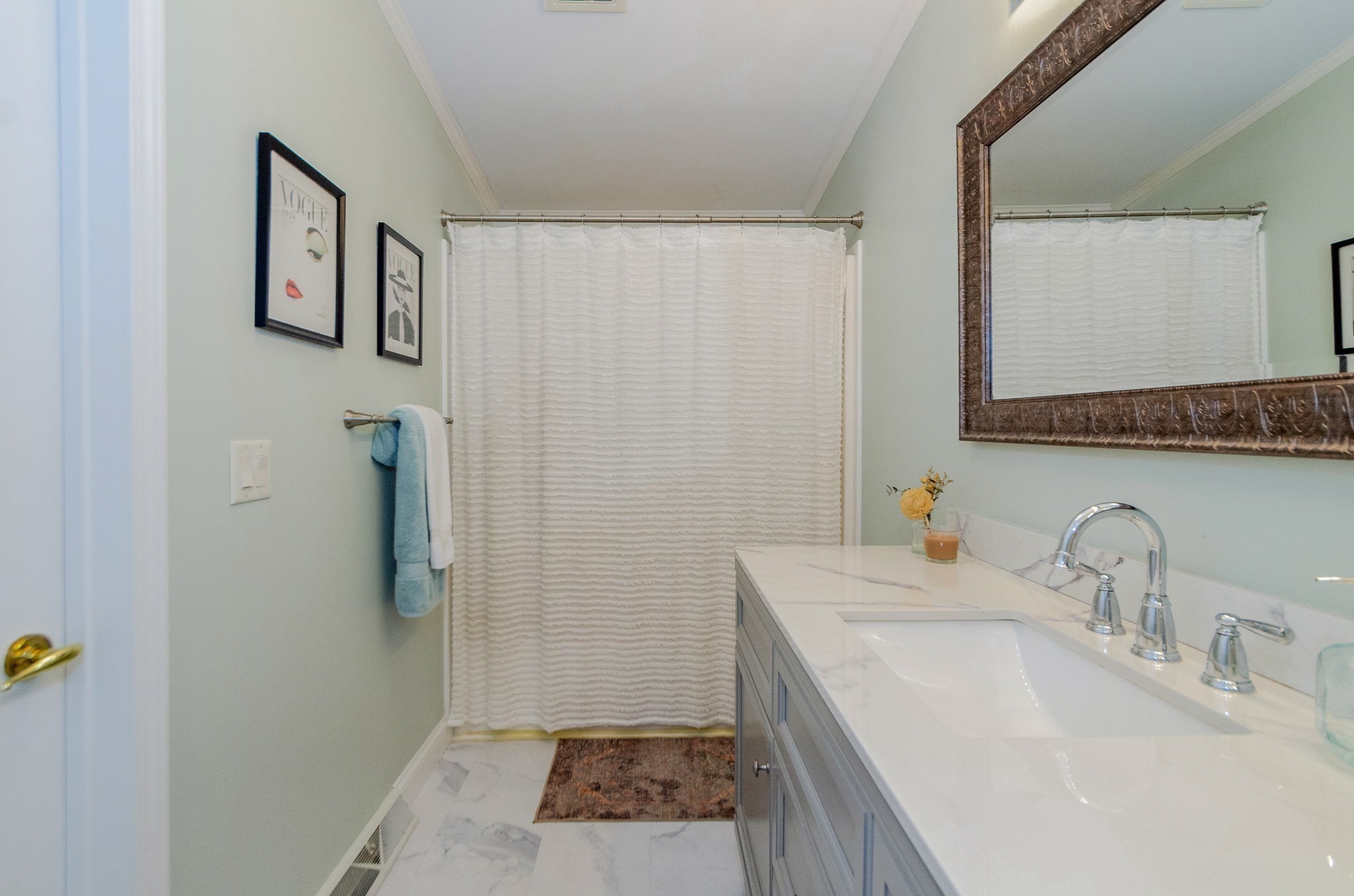 Bathroom with a gray vanity, white countertop, large framed mirror, and white shower curtain.